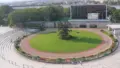 改修前の京都競馬場のパドックをグランドスワンA指定席から見下ろした風景で、円形の芝生と周回路の外側に観覧席が並び、奥に大型掲示板と森が見える俯瞰写真