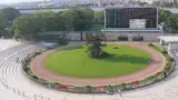 改修前の京都競馬場のパドックをグランドスワンA指定席から見下ろした風景で、円形の芝生と周回路の外側に観覧席が並び、奥に大型掲示板と森が見える俯瞰写真